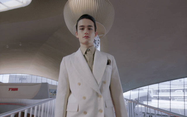 GIF of a woman in a tailored cropped blazer and skirt walking alongside a man in a white double-breasted suit.