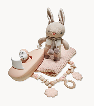 A pink blanket, rattle, plush toy rabbit and toy monkey in a boat 