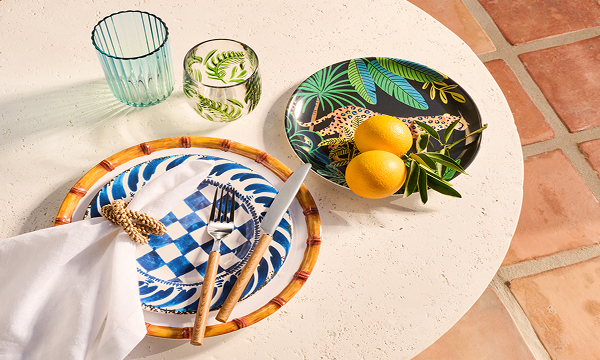 Table set with patterned plates, cutlery and a napkin, two glasses and a bowl with lemons. 