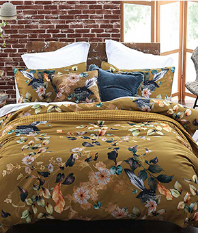 A double bed with a set of floral-print bedding against a contrasting brick wall