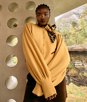 A female model wearing a butter yellow knit and matching silk scarf. 