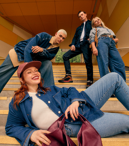 Four people pose on a staircase wearing denim outfits and casual footwear, with a burgundy leather bag in the foreground.