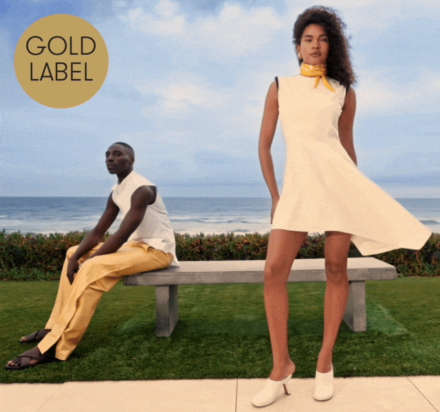 A GIF of a male and female model posing by a stone bench near the beach, wearing neutral outfits with the ocean behind them