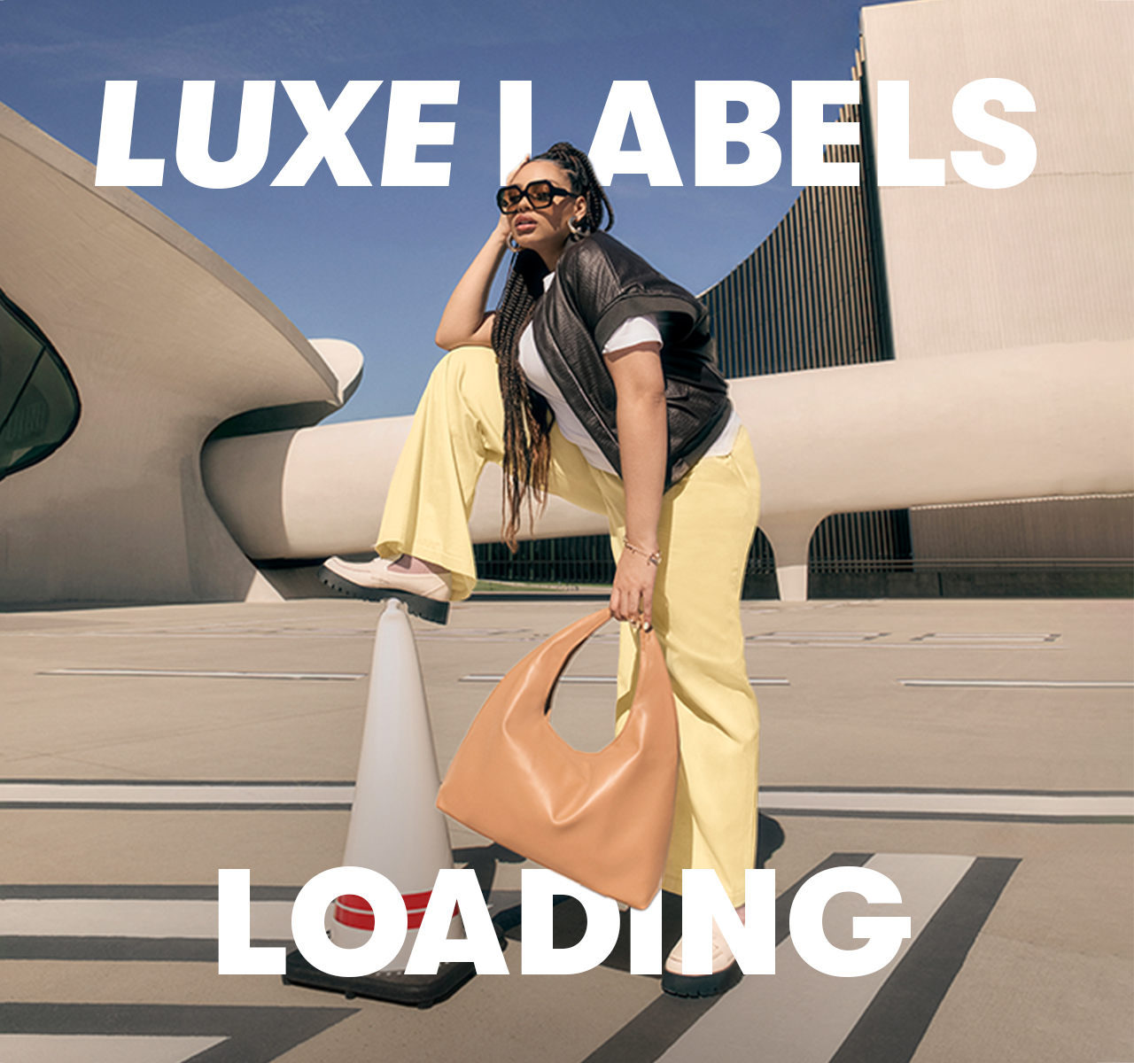A woman wearing a black top and yellow trousers, holding a large shoulder bag, with bold text reading “LUXE LABELS LOADING”.