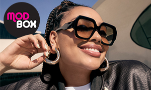 A smiling woman wearing statement sunglasses and big hoop earrings.
