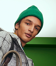 A man wearing a green knitted beanie and grey plaid coat.
