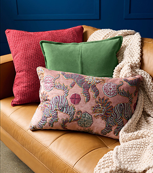 A selection of plush cushions on a leather sofa with a cosy knitted throw. 
