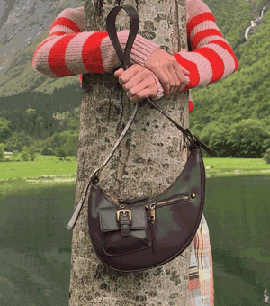GIF of a model standing next to a lake holding a leather bag