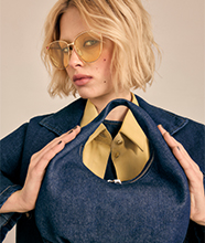 Woman in sunglasses holding a denim handbag.