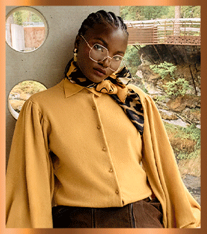 Woman wearing sunglasses, a scarf and yellow blouse.