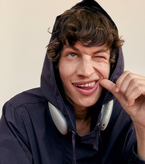 A close-up of a man wearing a navy blue hoodie with the hood over his ears and headphones around his neck.