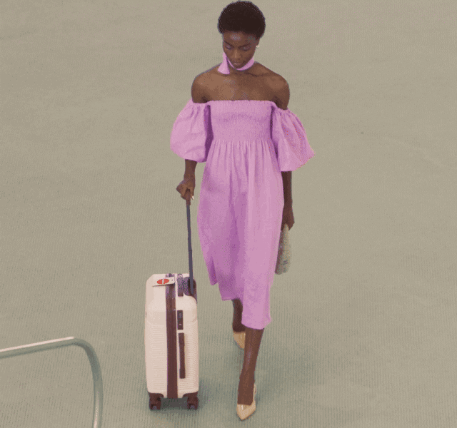 GIF of a model in a pink dress, wheeling a small suitcase.