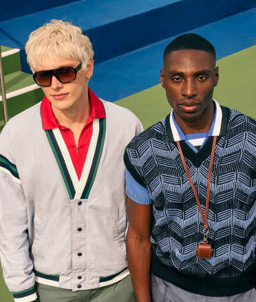 Two men standing side by side outdoors, wearing sunglasses and casual outfits. 