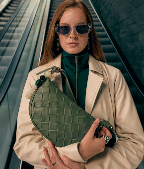 A model wearing statement sunnies with a woven olive-toned bag.