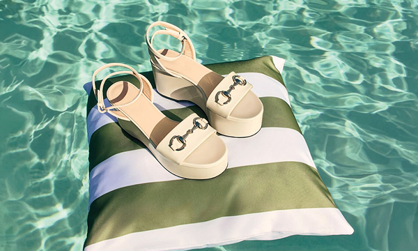 A pair of platform sandles with a horesebit detail float on an outdoor cusion, in a pool.