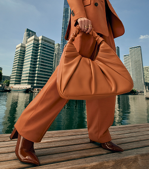 A woman wearing a burnt orange suit carrying a matching leather bag.