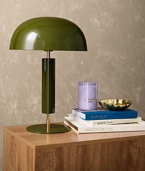 A green table lamp sitting on a sideboard alongside some books and a candle.