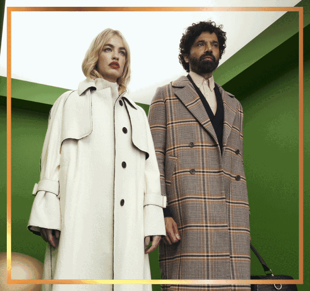 A woman wearing a cream sweater and trenchcoat standing beside a man wearing a cream shirt, black cardigan and plaid coat.