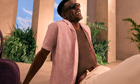 A male model smiling, wearing a light red shirt and sunglasses.