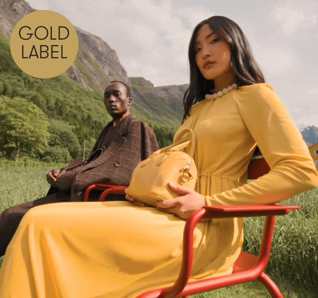 A female model wearing a long yellow dress and a male model in a brown suit sat on an Austrian hillside