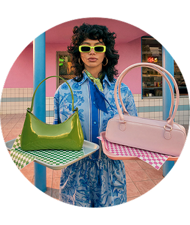Woman in sunglasses holding up a green and pink handbag.