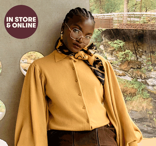 A female model wearing gold-framed glasses, a scarf, shirt with oversized sleeves and a suede skirt