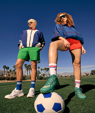 Two men sat on the sidelines of a tennic court in stylish outfits.