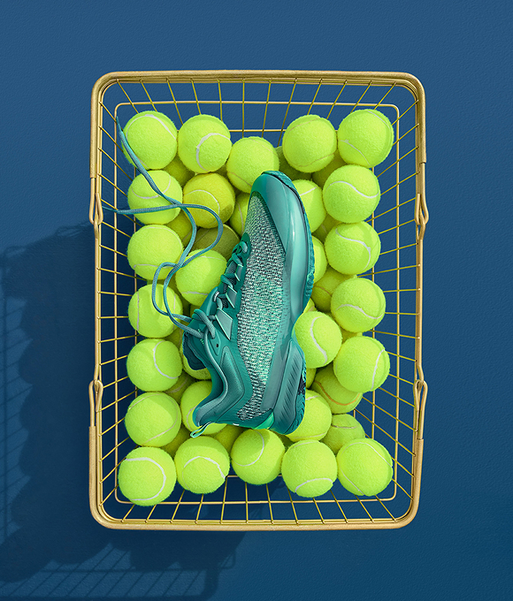 Teal trainer in a basket filled with tennis balls. 				