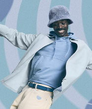 A smiling model wearing a bright blue shirt, a matching jacket and butter yellow trousers. 