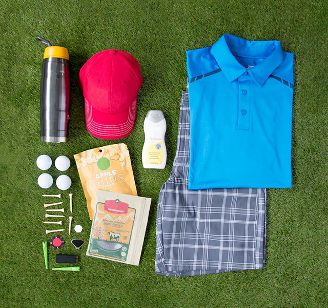 A selection of golf essentials including a polo shirt, golf balls and a cap – all placed on grass. 