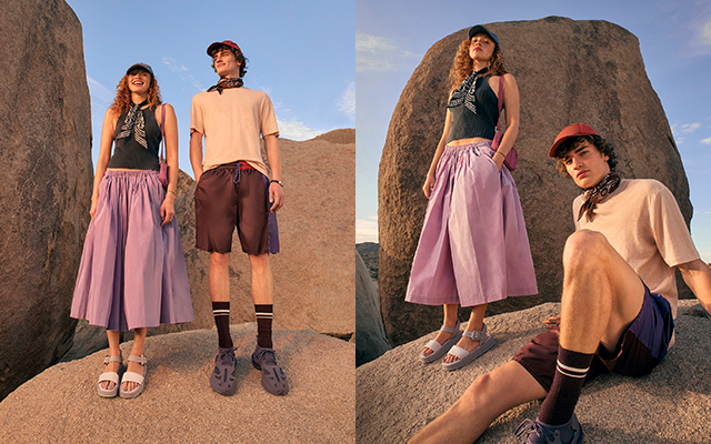 A man and woman stood on rocks wearing a sleeveless top with a lilac skirt and a light T‑shirt with dark shorts, both wearing caps and neckerchiefs.