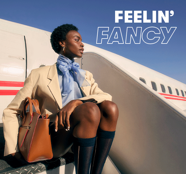 Woman sat on an aeroplane stairway wearing a cream blazer and blueblouse, and a man holding a brown leather satchel bag. Text reads 