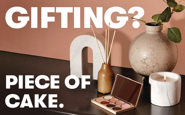 A desk with a makeup palette, marble white decor, brown diffuser and a lit candle on top.