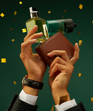 A man's hands holding up glass bottles of scent in a shower of glitter.