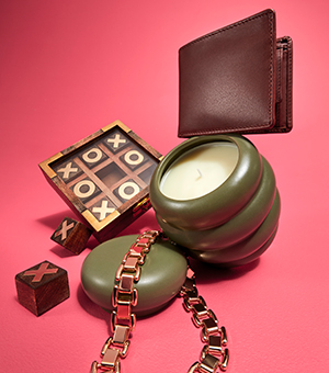 A wooden naughts and crosses board game, a brown wallet, a gold chain and an olive green candle.