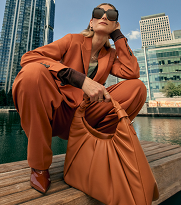 Woman wearing a rust-coloured suit and sunglasses, holding a matching handbag.