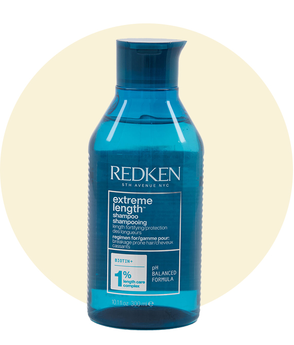 A blue bottle of Redken Extreme Length Shampoo stands against a pale yellow circle background, with clear text and branding visible on the label.