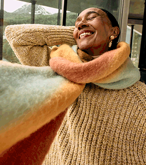 GIF alternating between an older female model wearing a mustard yellow fisherman's knit and scarf and a male model looking through binoculars.