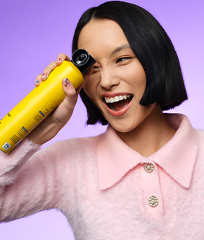 A female model wearing a pink top holding up a can of hairspray.