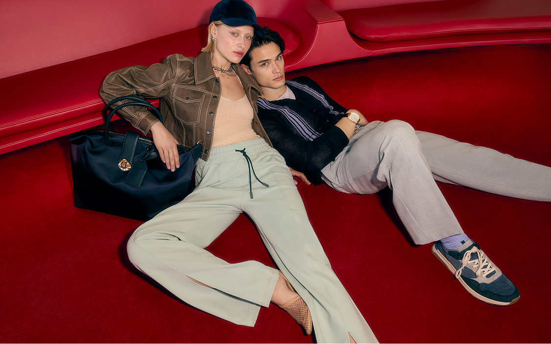 A man and woman wearing casual clothing and accessories, seated on a red carpeted set.