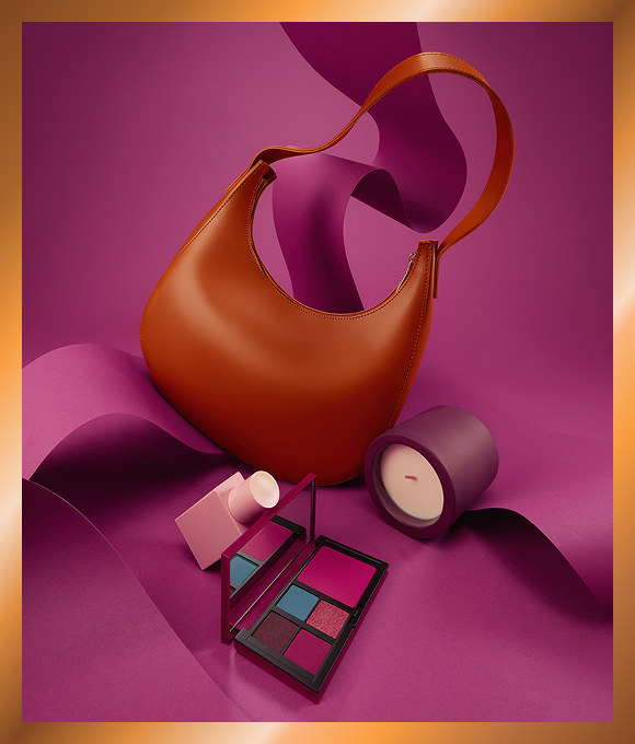 Handbag, makeup pallet and candle against purple background.