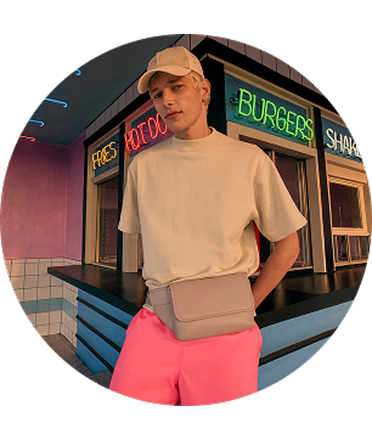 A man in a cap and pink shorts with crossbody bag.