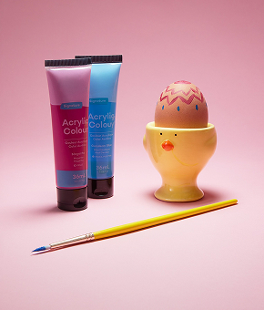 A freshly decorated egg sits in an egg cup, alongside colourful paints and a paintbrush.